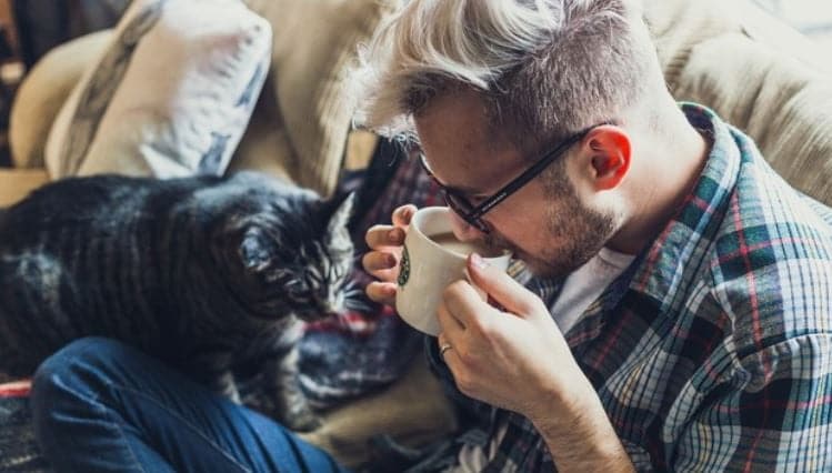 Man drinking coffee on the couch with cat